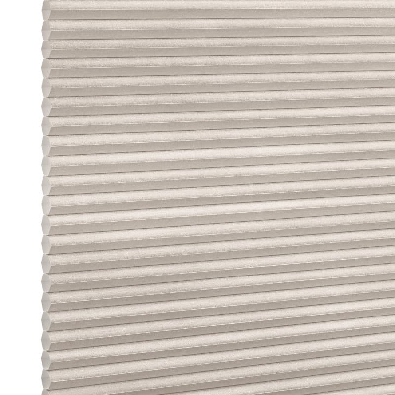 Beige cellular (honeycomb) blind, horizontal pleats with visible hexagonal cells at left edge; closed and diffusing light; photographed in a neutral, evenly lit studio setting with no visible room.