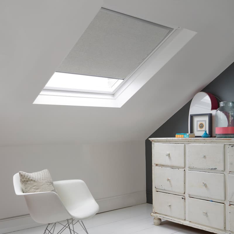 Room with white eaves wall, dark blue-grey wall to right with a shabby chic white drawer unit, a contemporary white chair, white painted floorboards and a skylight blind in pale flint grey.