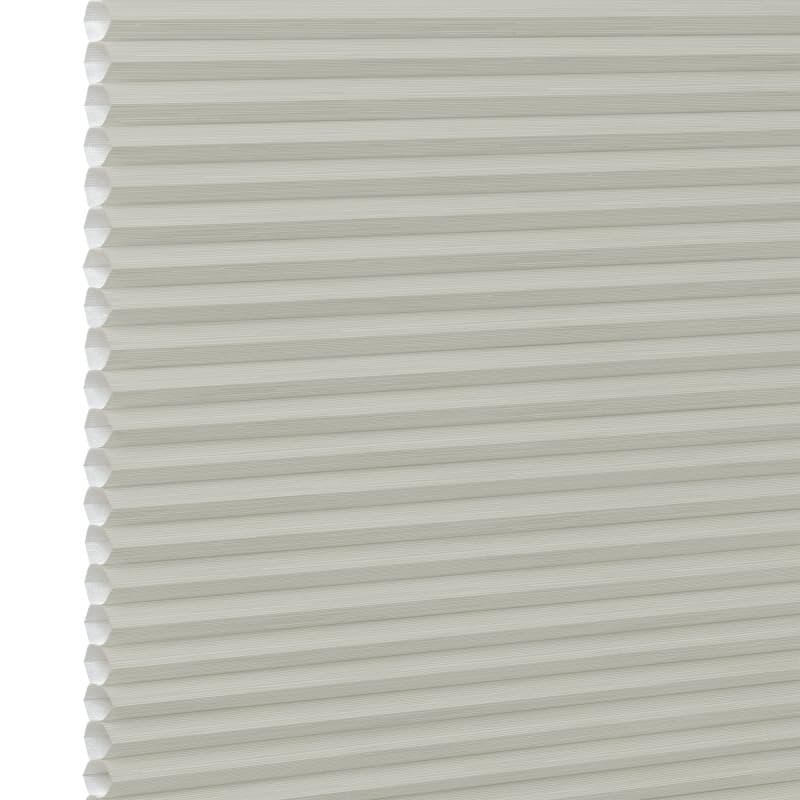 Cream cellular (honeycomb) window blind, fully lowered with visible hexagonal pleats at the left edge; closed and diffusing light; close-up against a plain white background with soft lighting.