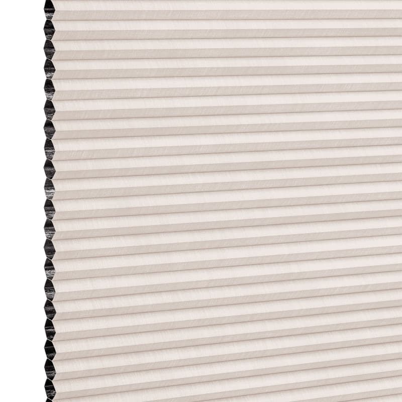 Beige pleated honeycomb cellular blind, fully lowered with visible black cells along the left edge; filtering light in a close-up studio view of the shade surface.