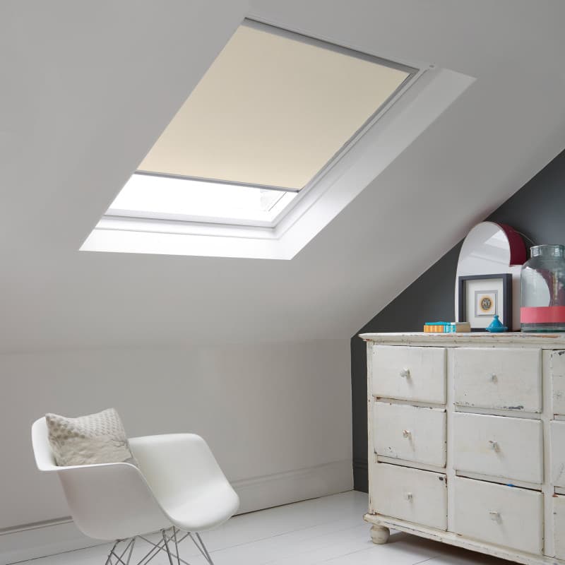 Room with white eaves wall, dark blue-grey wall to right with a shabby chic white drawer unit, a contemporary white chair, white painted floorboards and a skylight blind in cream.