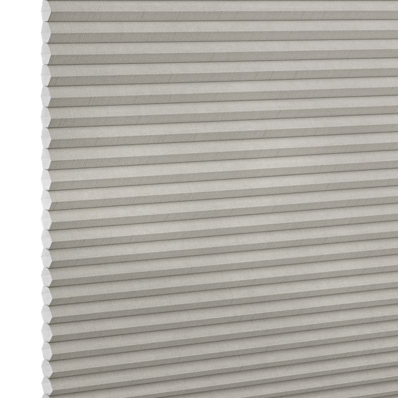 Light-gray pleated cellular window shade, closed with visible honeycomb cells and fabric texture; blocking light and insulating; shown close-up against a neutral, evenly lit backdrop.