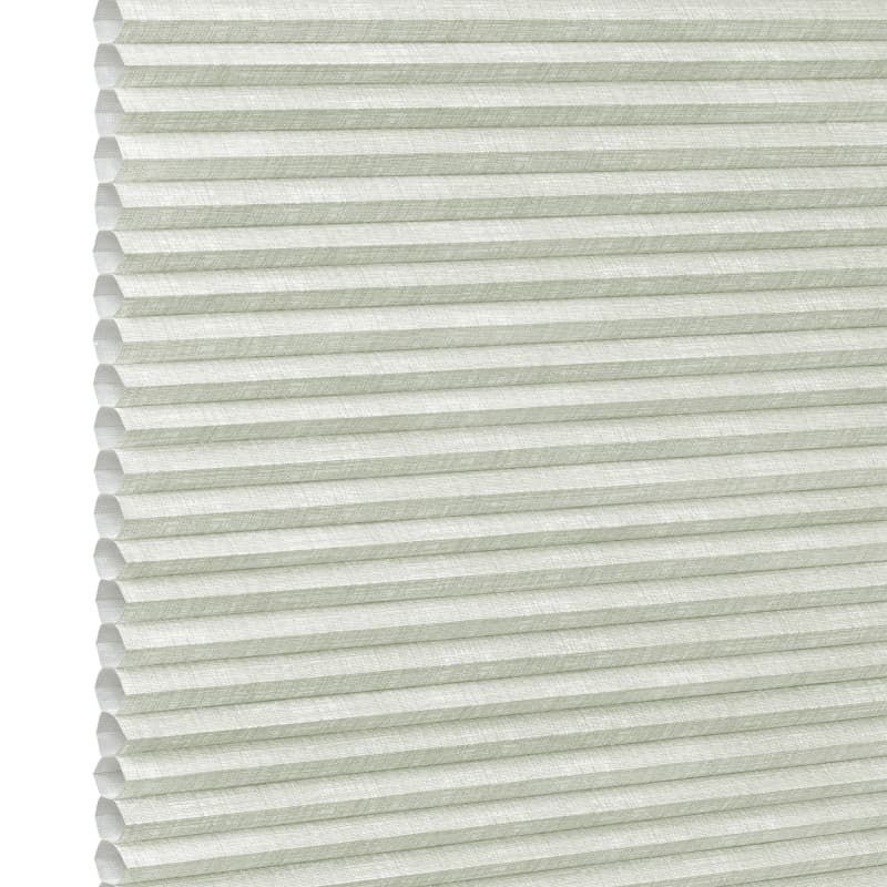 Pale green honeycomb (cellular) blind, fully lowered with visible hexagonal cells and textured fabric; closed, gently diffusing daylight; fills the frame against a bright neutral background suggesting an interior window.