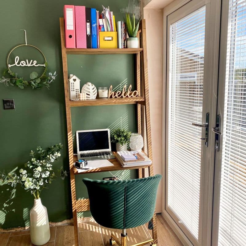 Horizontal white venetian blinds on glass patio doors, slats tilted, filtering sunlight into narrow striped shadows. Adjacent home-office nook with wooden ladder-shelf, laptop, green painted wall and velvet chair.

hello
love
