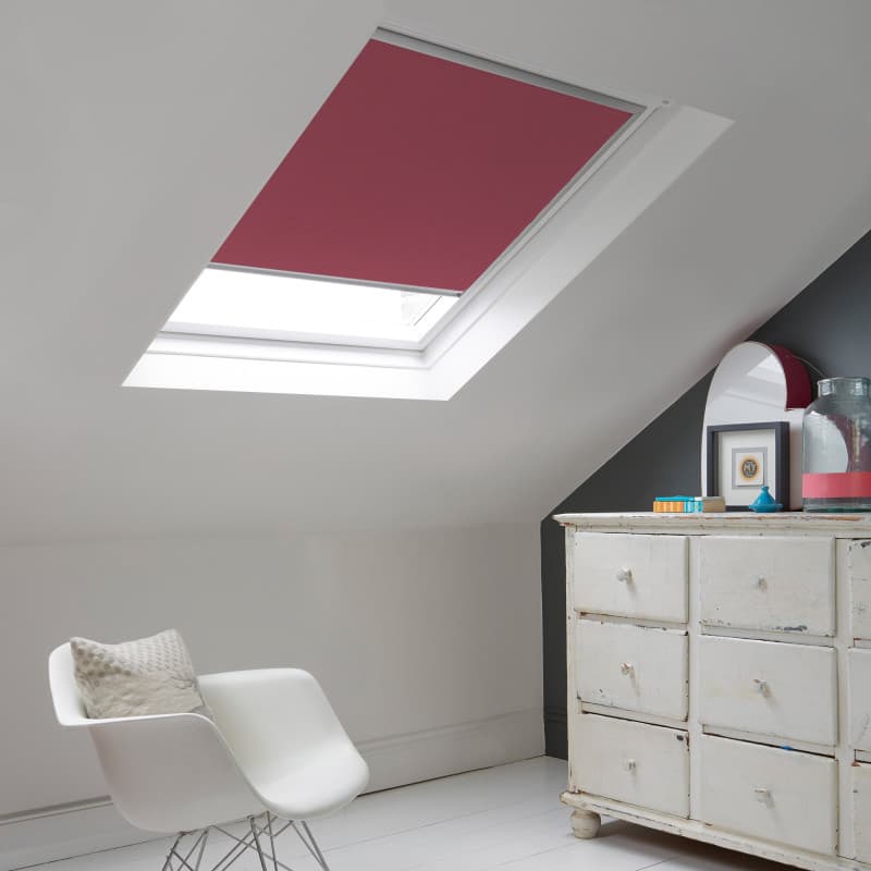 Room with white eaves wall, dark blue-grey wall to right with a shabby chic white drawer unit, a contemporary white chair, white painted floorboards and a skylight blind in pale raspberry.