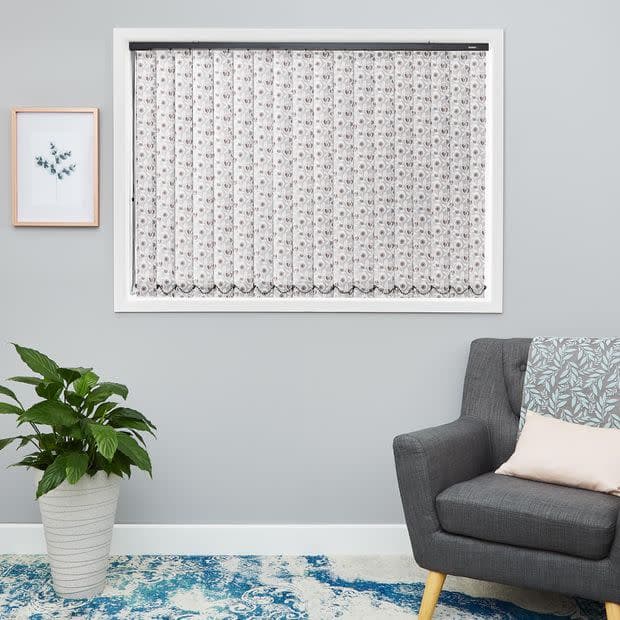 Sheer white lace curtain, fitted inside the window frame with floral pattern and scalloped hemâ€”hanging closed, softly filtering daylight in a light-gray living room with gray armchair, potted plant, and blue rug.