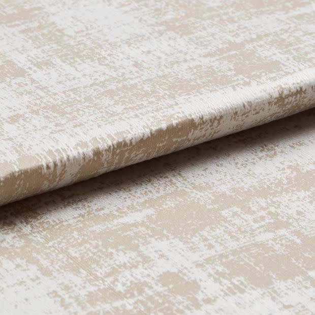 Beige-and-white distressed-pattern fabric panel with a horizontal fold, resembling a Roman blind; photographed close-up on a neutral surface under soft, even lighting.