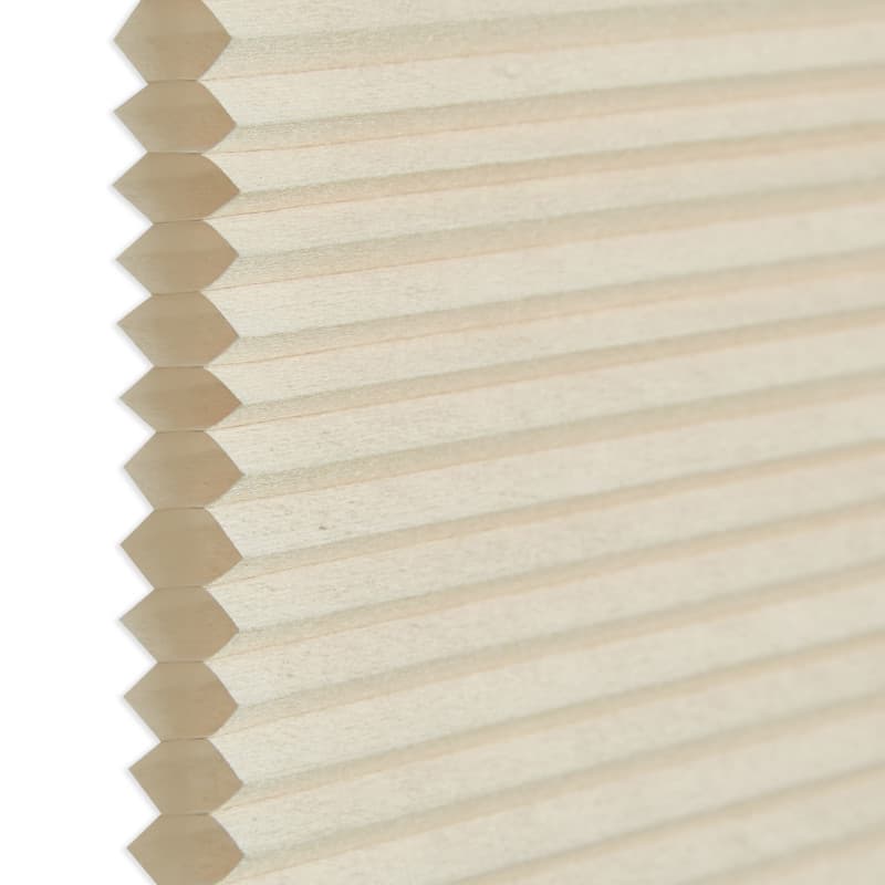 Honeycomb cellular blind, beige pleated fabric with visible hexagonal cell edges at left; closed and flat. Close-up against a neutral white background with soft, diffused indoor lighting.