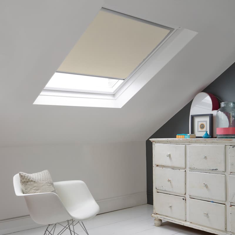 Room with white eaves wall, dark blue-grey wall to right with a shabby chic white drawer unit, a contemporary white chair, white painted floorboards and a skylight blind in cappucino.