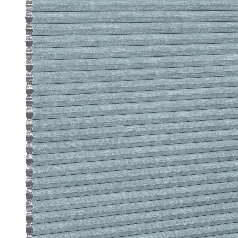 Light-blue textured cellular (honeycomb) pleated shade, tightly closed showing hexagonal cell edges at left; blocking light and insulating a window within a softly lit interior, neutral background.