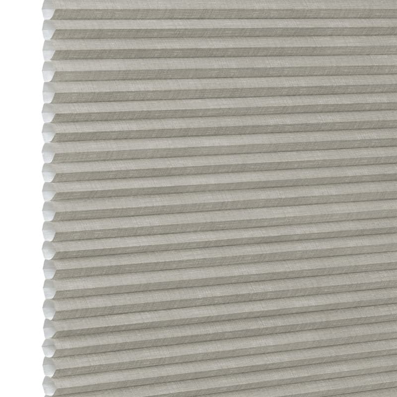 Honeycomb cellular fabric blind with horizontal pleats and textured beige finish, fully lowered and closed, diffusing soft light; set against a neutral, evenly lit wall with narrow white margin left.