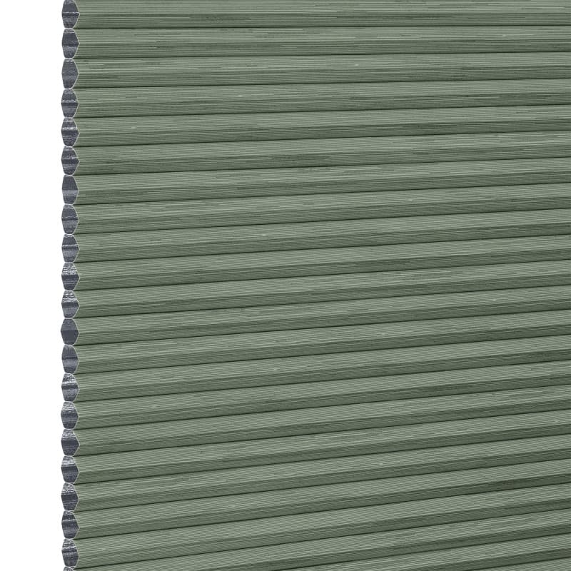 Cellular honeycomb blind â€” sage-green pleated fabric fully lowered with exposed hexagonal cells along the left edge; blocking and softly filtering light in a neutral interior.