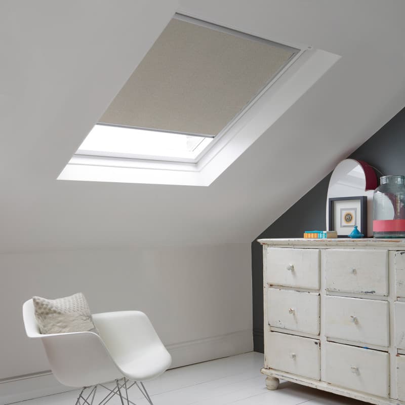 Room with white eaves wall, dark blue-grey wall to right with a shabby chic white drawer unit, a contemporary white chair, white painted floorboards and a skylight blind in pale grey with a subtle glitter effect.