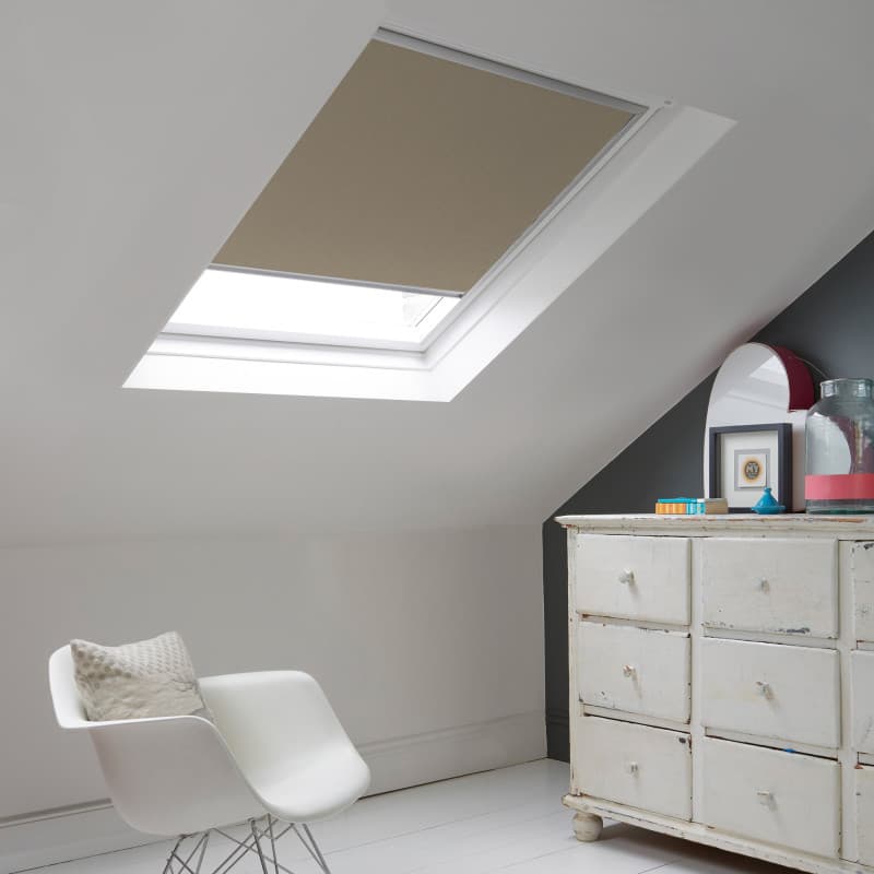 Room with white eaves wall, dark blue-grey wall to right with a shabby chic white drawer unit, a contemporary white chair, white painted floorboards and a skylight blind in taupe.