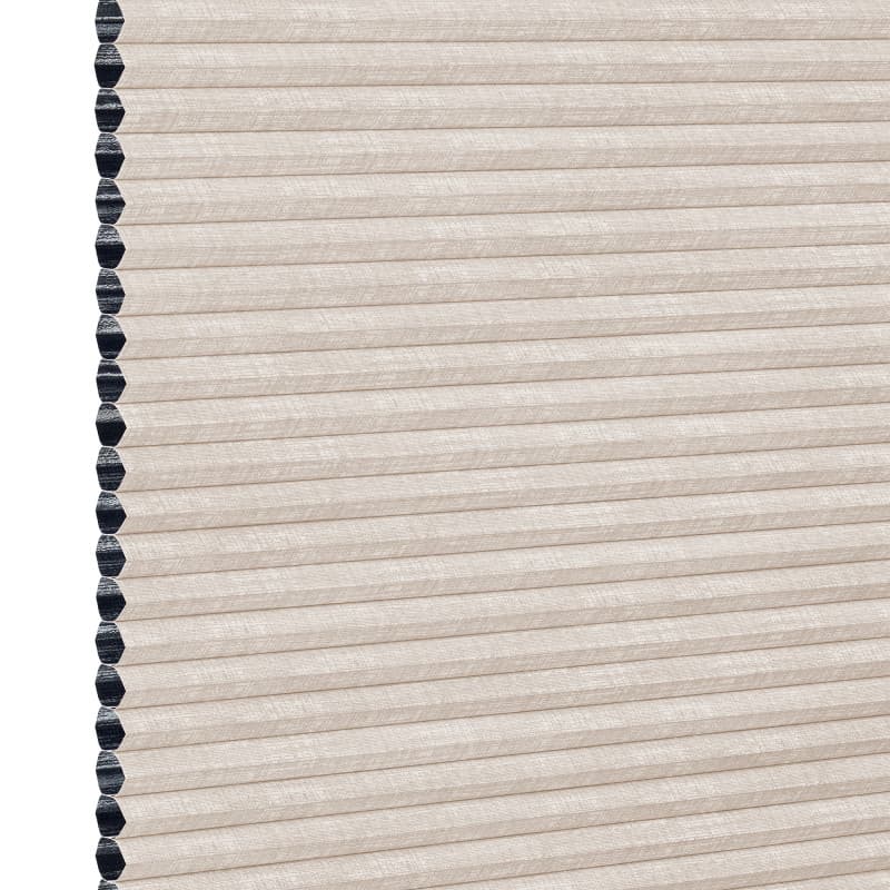 Beige cellular (honeycomb) window shade, pleated and fully lowered with exposed black cell openings along the left edge, blocking light and showing a textured fabric surface against a white background.
