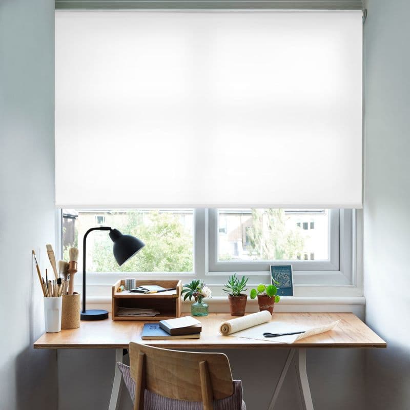 White roller blind, lowered across a double window, opaque and diffusing bright daylight; covering most of the pane above a tidy wooden desk with lamp, brushes, potted succulents, and suburban view.

"British Herbs"