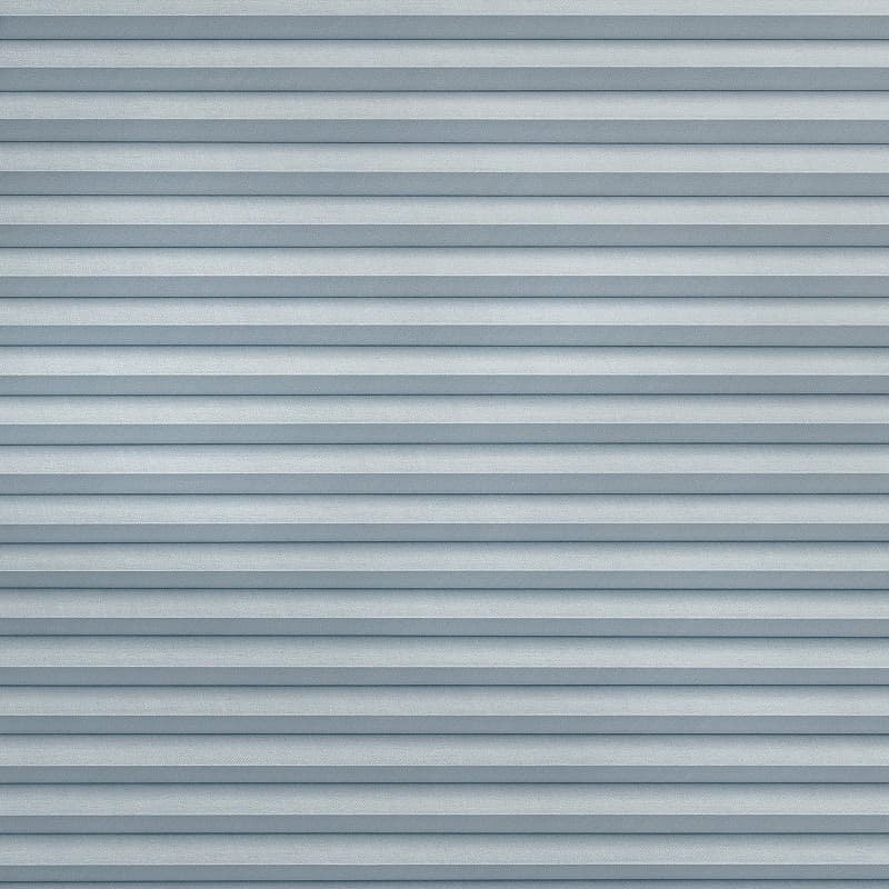 Horizontal pleated fabric blinds covering the entire window, closed in even light-blue-gray folds; filtering and diffusing daylight; interior setting with soft, uniform ambient lighting and no visible view.
