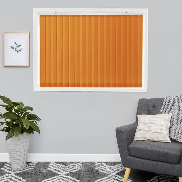 Vertical orange blinds fully closed across a white-framed window, blocking light; modern living room with gray walls, a gray upholstered armchair, patterned rug, potted plant and small framed art.