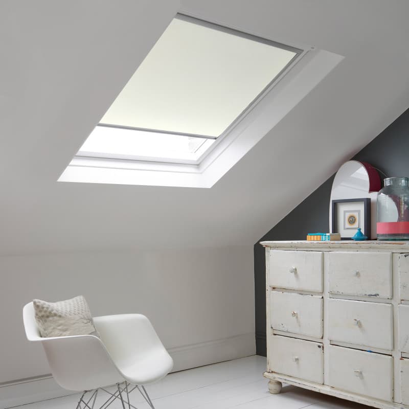 Room with white eaves wall, dark blue-grey wall to right with a shabby chic white drawer unit, a contemporary white chair, white painted floorboards and a skylight blind in opal.
