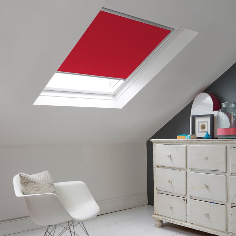 Room with white eaves wall, dark blue-grey wall to right with a shabby chic white drawer unit, a contemporary white chair, white painted floorboards and a skylight blind in pale red.