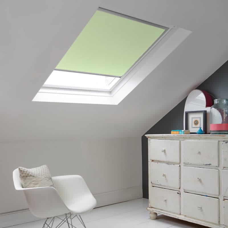 Room with white eaves wall, dark blue-grey wall to right with a shabby chic white drawer unit, a contemporary white chair, white painted floorboards and a skylight blind in pale sea green.