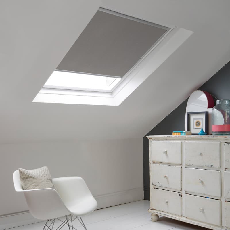 Room with white eaves wall, dark blue-grey wall to right with a shabby chic white drawer unit, a contemporary white chair, white painted floorboards and a skylight blind in pale slate grey.