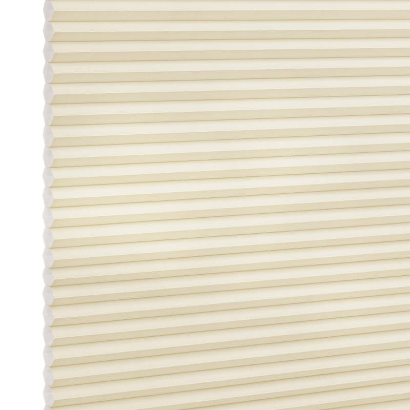 Cream-colored cellular (honeycomb) blind, fully lowered and closed, pleated horizontal cells; gently filtering diffuse light against a plain, softly lit interior with no visible window frame.