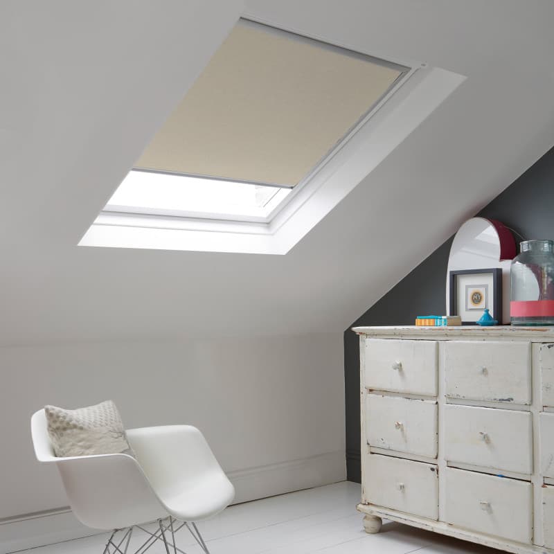 Room with white eaves wall, dark blue-grey wall to right with a shabby chic white drawer unit, a contemporary white chair, white painted floorboards and a skylight blind in pale mushroom.