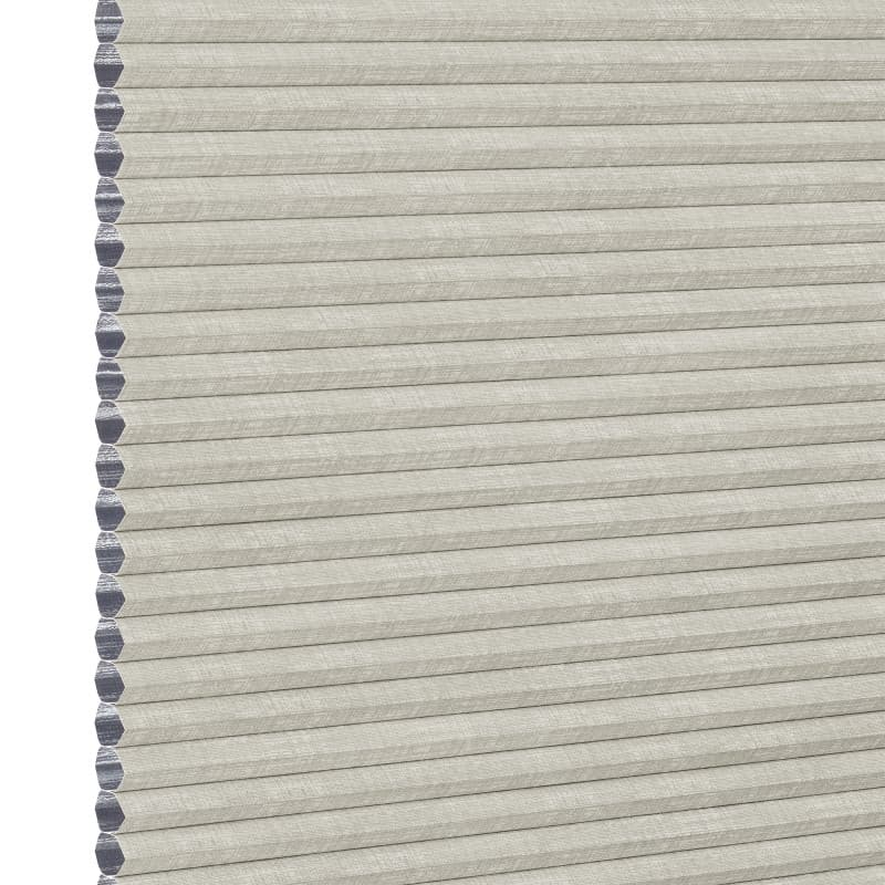 Light beige honeycomb cellular shade with pleated fabric and exposed hexagonal cell ends at left, fully lowered and closed, concealing view; close-up product-style shot on white background with even lighting.