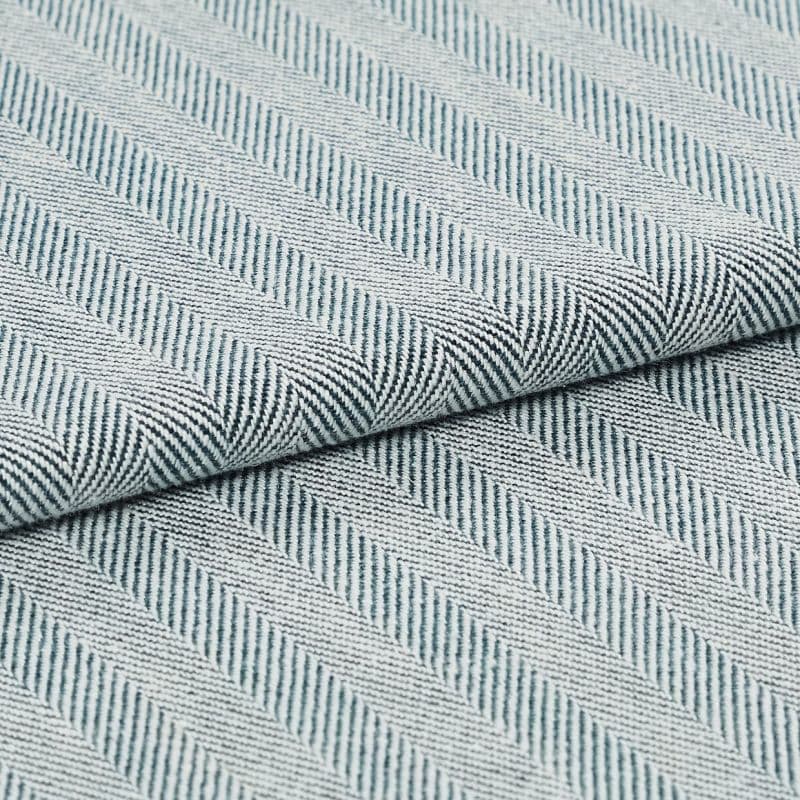 Folded woven textile with diagonal raised ribbed stripes in pale blue and white; fabric overlapped along a central fold; close-up view with soft, even lighting on a neutral surface.