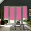 Pink roller blinds cover French doors and sidelights, blocking light; they hang above a glass coffee table in a living room with green armchairs, chevron rug, and potted plants.