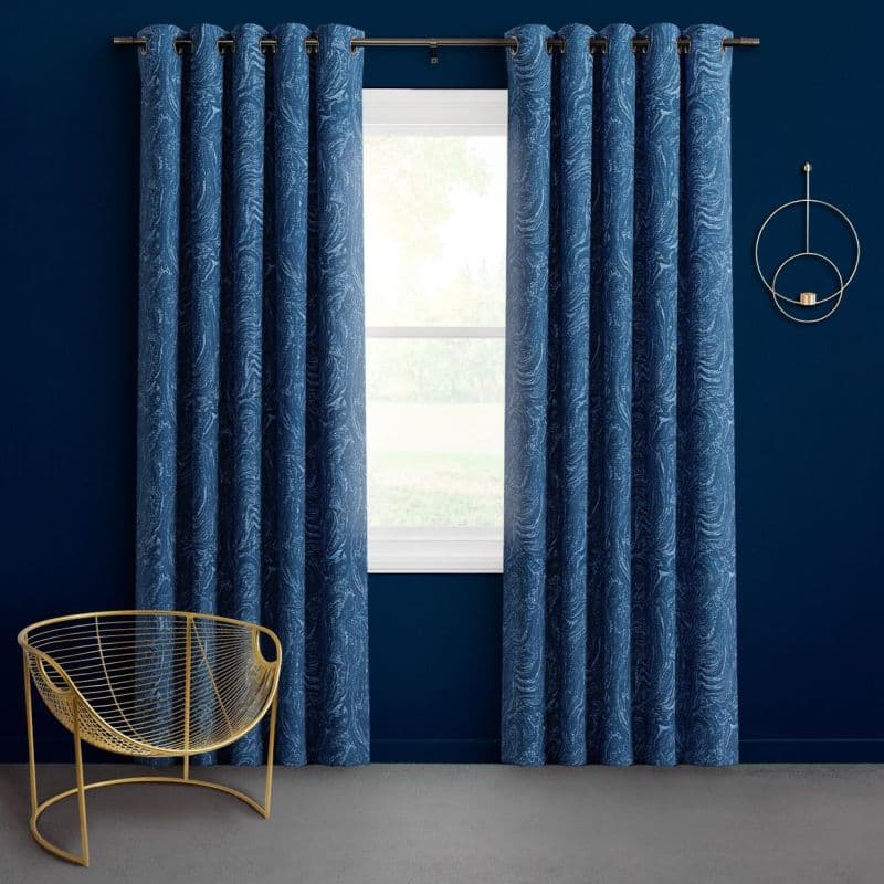 Blue grommet curtains, marbled swirl, hung on a rod and parted to frame a central window; filtering daylight; dark-blue room with a gold wire chair and circular wall décor.