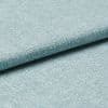 Light-blue woven upholstery fabric folded so one edge overlaps, revealing tight textured weave; photographed as a close-up on a flat surface with soft, even studio lighting for a material sample.