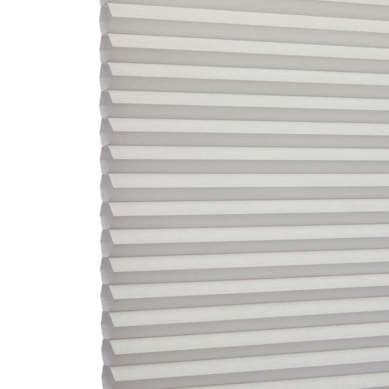 White cellular (honeycomb) blind, left-edge visible with uniform horizontal pleats; fully lowered and closed, softly filtering daylight; set against a bright, neutral interior background.