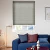 Gray pleated blind lowered over a window, filtering daylight; in a bright living room with blue sofa topped by navy and burgundy cushions, brass floor lamp and abstract wall art.