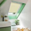 Cream pleated skylight blind lowered, filtering daylight; in a bright attic bathroom with mint-green window trim, white herringbone tiles, sink, bathtub, plant and toiletries on shelves.