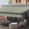 Striped retractable fabric awning, green and beige diagonal stripes, fully extended over patio; shading the sliding glass doors and outdoor seating area with modern chairs, wooden table, and daytime light.