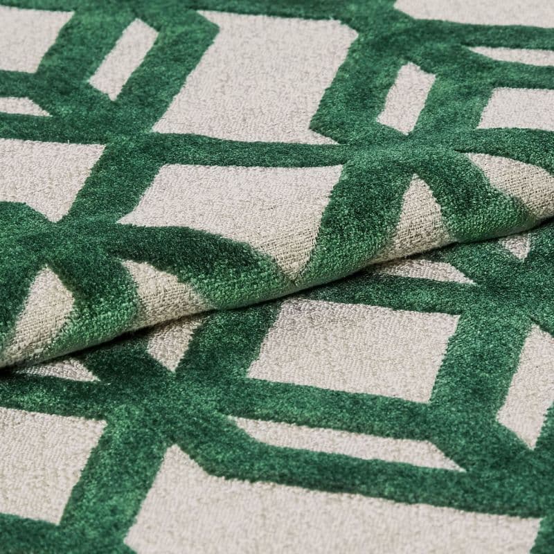 Tufted rug with raised green geometric lattice on a beige ground — folded to show pile and backing — close-up, studio-lit textile sample highlighting textured fibers and overlapping layers.