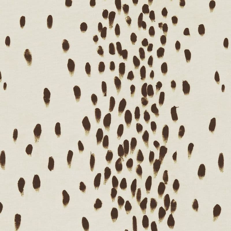 Cream fabric patterned with irregular brown brushstroke ovals — clustered centrally and scattered outward — covering a flat surface under even, neutral lighting, resembling abstract textile or wallpaper.