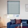 Light-blue cellular blind, lowered over most of the window with a narrow bottom gap, filtering daylight; contemporary living room with blue sofa, mixed cushions, brass floor lamp, framed wall art.