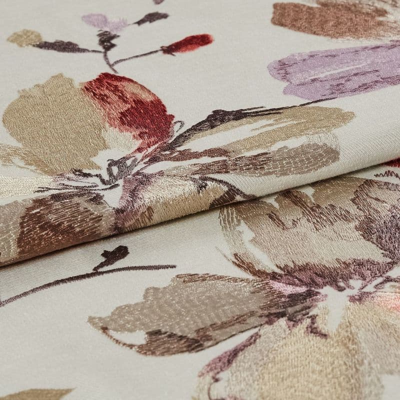 Folded cream jacquard fabric with metallic beige, mauve and red floral motifs — layered to reveal raised sheen and woven texture — close-up on flat surface under soft, even lighting.
