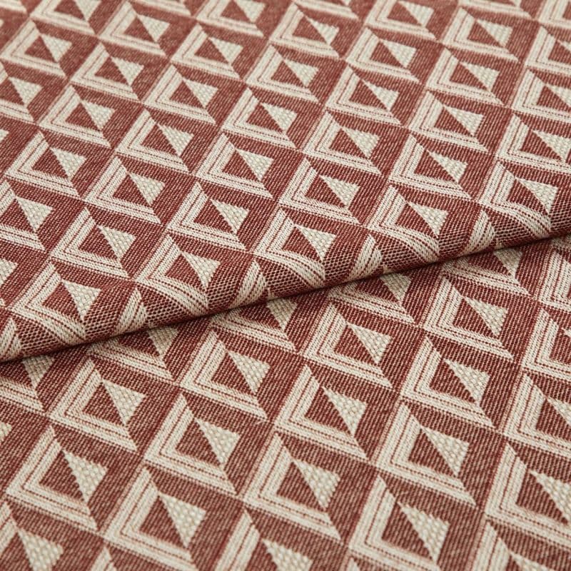 Woven upholstery fabric with repeating terracotta-and-cream triangular motif, folded once across the frame, revealing textured weave and raised pattern; close-up, evenly lit studio shot on neutral surface.