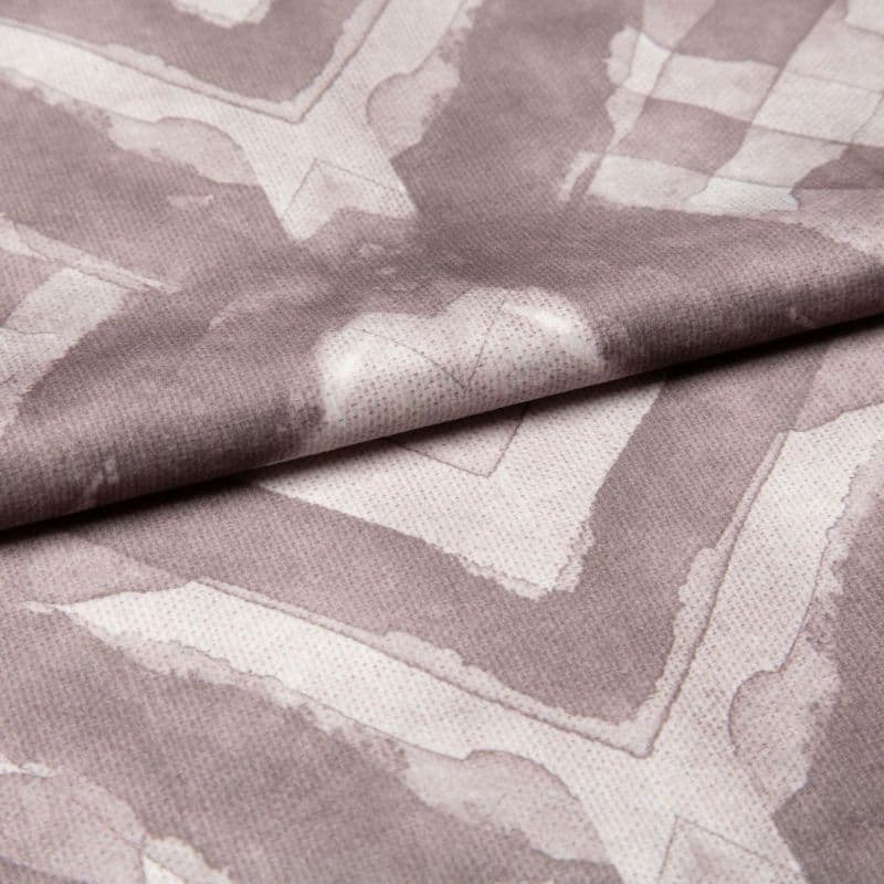 Soft woven fabric with faded mauve geometric frames and subtle heart motif (folded across the center), draped and overlapped to reveal stitched texture, close-up under even studio lighting.