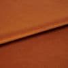 Copper-orange satin fabric, folded with visible edge, reflecting light — close-up studio shot showing soft sheen, fine texture, and warm even lighting.