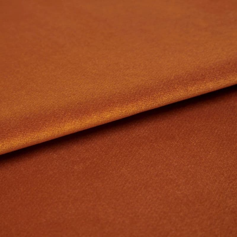Copper-orange satin fabric, folded with visible edge, reflecting light — close-up studio shot showing soft sheen, fine texture, and warm even lighting.