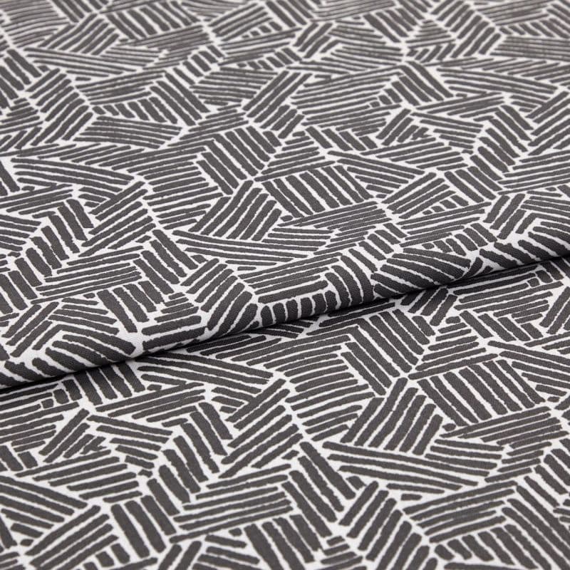 Folded patterned fabric: gray-and-white geometric print of short parallel stripes forming irregular polygons, folded across the middle. Close-up on flat surface with even studio lighting.