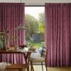 Full-length pleated velvet curtains, deep mauve, drawn open slightly at center to frame and filter daylight through a sliding glass door; dining table with pendant lamp, plates of pancakes, garden beyond.