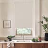 Roller blind lowered over a window above a kitchen sink, filtering light; countertop displays faucet and sink, bowl of leafy greens, potted plants, and a framed sketch on pale walls.