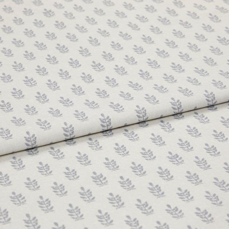 Light-coloured cotton fabric with repeating small grey leaf motifs, folded across the middle, shown in a soft, evenly lit studio close-up.