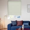 Pale green cellular (honeycomb) blind, lowered over most of a sash window with subtle horizontal ribs, filtering daylight; living room with blue sofa, assorted cushions, floor lamp and framed art.